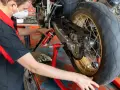 Meccanico con mascherina esegue la pulizia motore e lubrificazione catena moto su cavalletto.