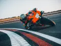Un pilota con tuta arancione e casco decorato piega in curva su una KTM su una pista da corsa.
