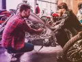 Due uomini esaminano un motore di moto custom. Uno mostra all'altro i dettagli, forse discutendo il costo della messa in strada della moto.