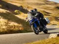 Coppia su una moto per due persone sfreccia su una strada panoramica tra colline dorate.