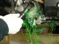 Mano con guanto bianco che scollega un tubo, facendo fuoriuscire liquido verde brillante per il cambio del liquido radiatore.