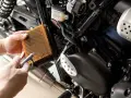 Mani puliscono il filtro dell'aria di una moto con aria compressa. Un filtro pulito è essenziale per il corretto funzionamento del motore, garantendo che a cosa serve il filtro dell'aria.