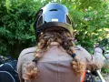 Donna con casco nero e capelli raccolti in due trecce, pronta a legare il casco alla moto.