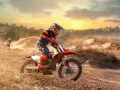Un pilota di **enduro motocross** sfreccia su un terreno polveroso al tramonto, sollevando terra.