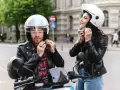 Coppia in moto, entrambi indossano un casco integrale. Lui con camicia a quadri, lei con giacca di pelle.