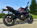 Moto SRK 700 color bronzo e nero, parcheggiata all'aperto con cielo azzurro e verde.