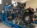 Officina BMW: moto smontata su sollevatore, in attesa del raffreddamento motore. Attrezzi e meccanico al lavoro.