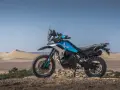 Moto blu e nera, perfetta per avventura e viaggi, posizionata su un terreno sabbioso con dune all'orizzonte.