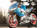 Aprilia carenata blu e rossa, con cerchi rossi, pronta per sfrecciare su pista.
