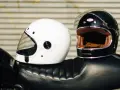 Due caschi integrali, uno bianco e uno nero, appoggiati sul sedile di una moto. Il peso del casco integrale è un fattore importante per il comfort.
