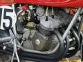 Dettaglio del motore di una moto da corsa, con il numero 15 su un cerchio bianco. Il motore è un complesso di tubi e metallo, pronto a ruggire.