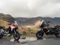 Due moto, una Ducati Multistrada 1290 rossa e bianca e una KTM 1290 Super Adventure nera e arancione, parcheggiate su una strada di montagna con un paesaggio nebbioso sullo sfondo.
