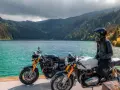 Due moto da enduro, una nera e una bianca, con una donna in sella, godono del panorama di un lago alpino.