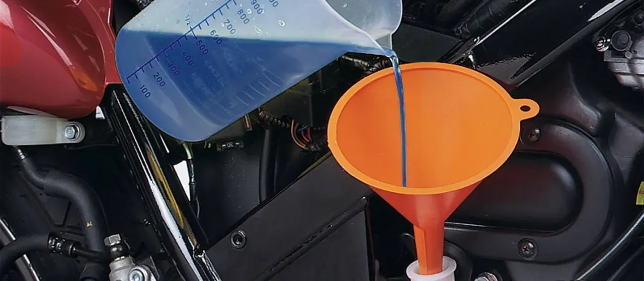 Versando liquido refrigerante blu in un imbuto arancione per diluirlo.