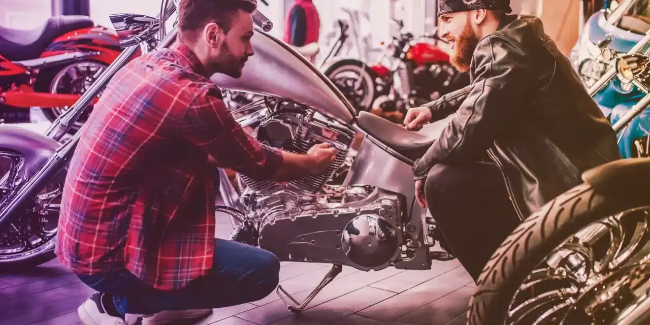 Due uomini esaminano un motore di moto custom. Uno mostra all'altro i dettagli, forse discutendo il costo della messa in strada della moto.