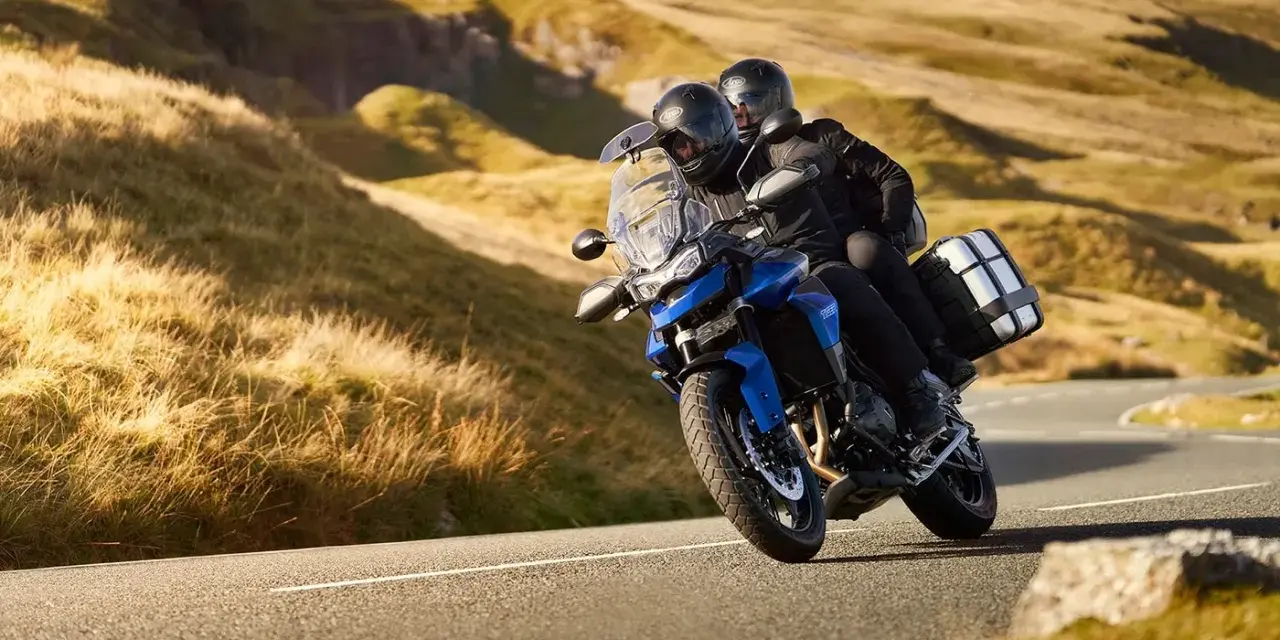 Coppia su una moto per due persone sfreccia su una strada panoramica tra colline dorate.