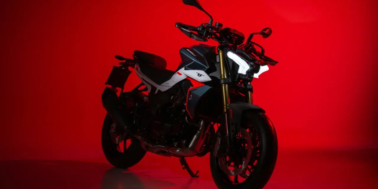 La Benelli TNT 500, con il suo design aggressivo e i fari a LED luminosi, si staglia su uno sfondo rosso acceso, pronta a conquistare la strada.
