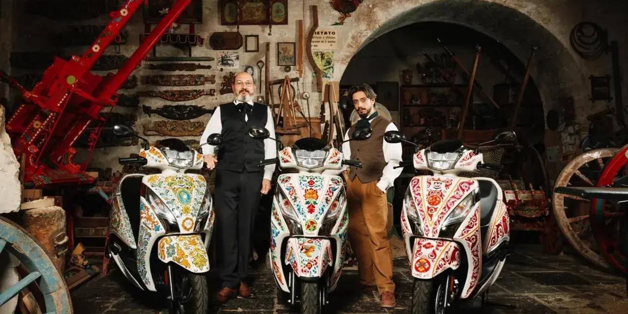 Due uomini in abiti tradizionali posano con tre scooter decorati. Uno scooter non si accende il quadro, ma l'arte sui veicoli è vibrante.