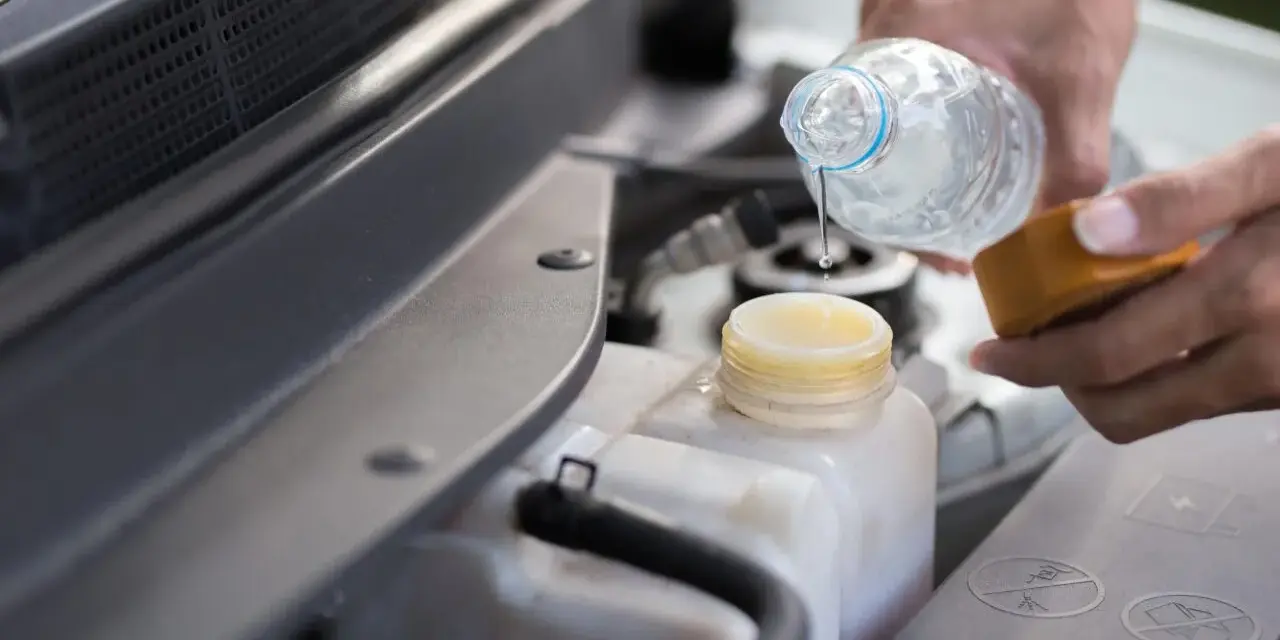 Mani versano acqua nel serbatoio del liquido di raffreddamento dell'auto, assicurandosi che ci sia acqua nel radiatore.