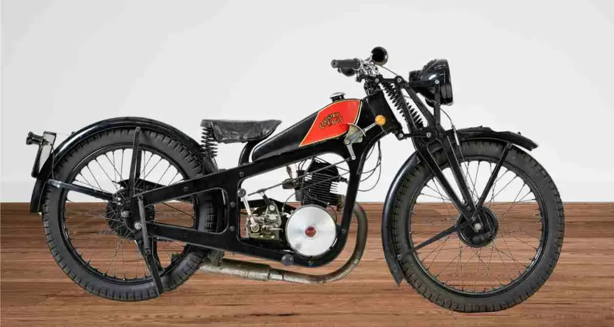 Una rara moto d'epoca, nera con serbatoio rosso e logo, su un pavimento di legno.