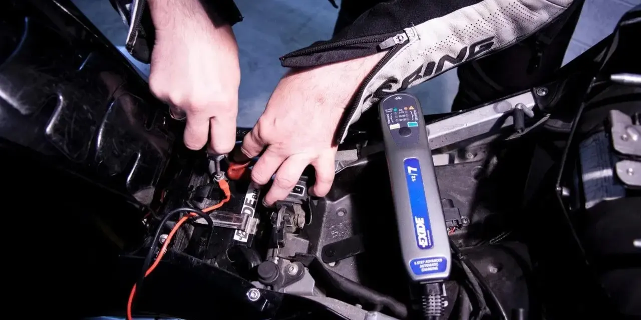 Mani che collegano un caricabatterie Exide a una batteria di moto. La batteria non tiene la carica, quindi si prova a ricaricarla.