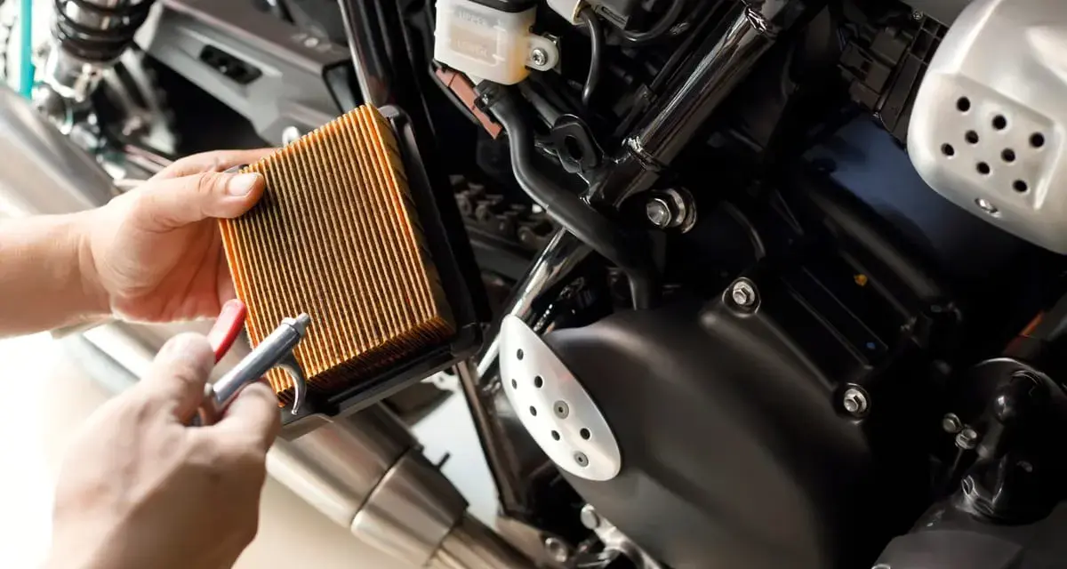 Mani puliscono il filtro dell'aria di una moto con aria compressa. Un filtro pulito è essenziale per il corretto funzionamento del motore, garantendo che a cosa serve il filtro dell'aria.