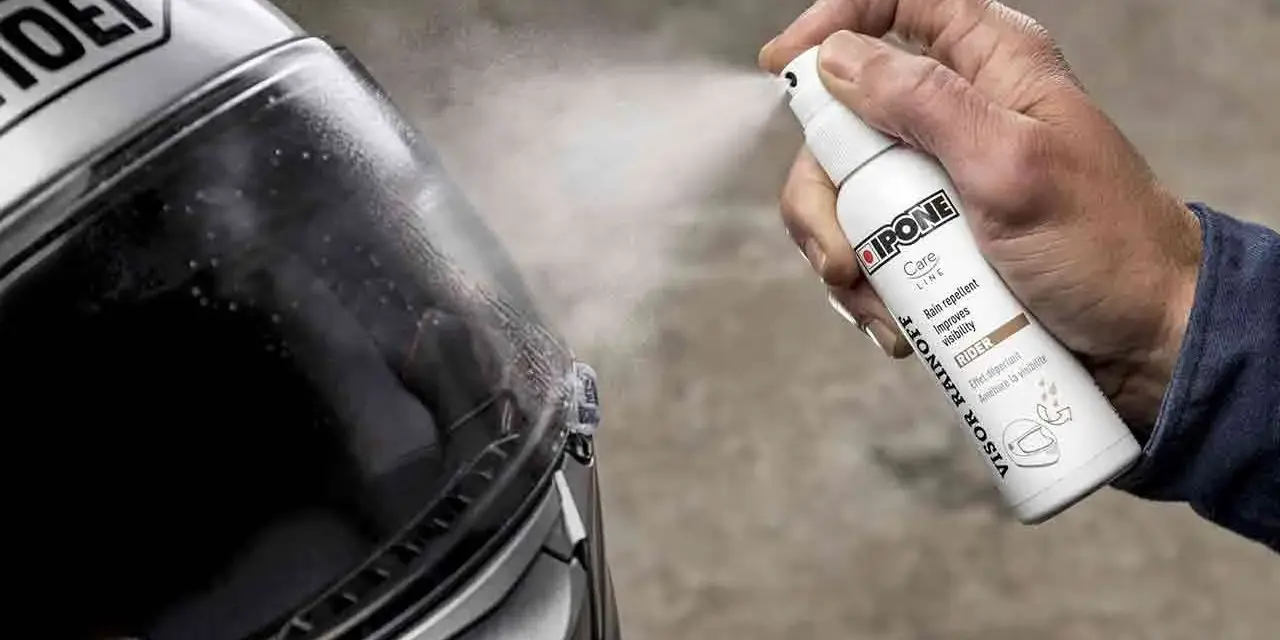 Mano spruzza spray idrorepellente sul casco Shoei. Il casco non deve essere pulito con benzina, ma con prodotti specifici per la visiera.