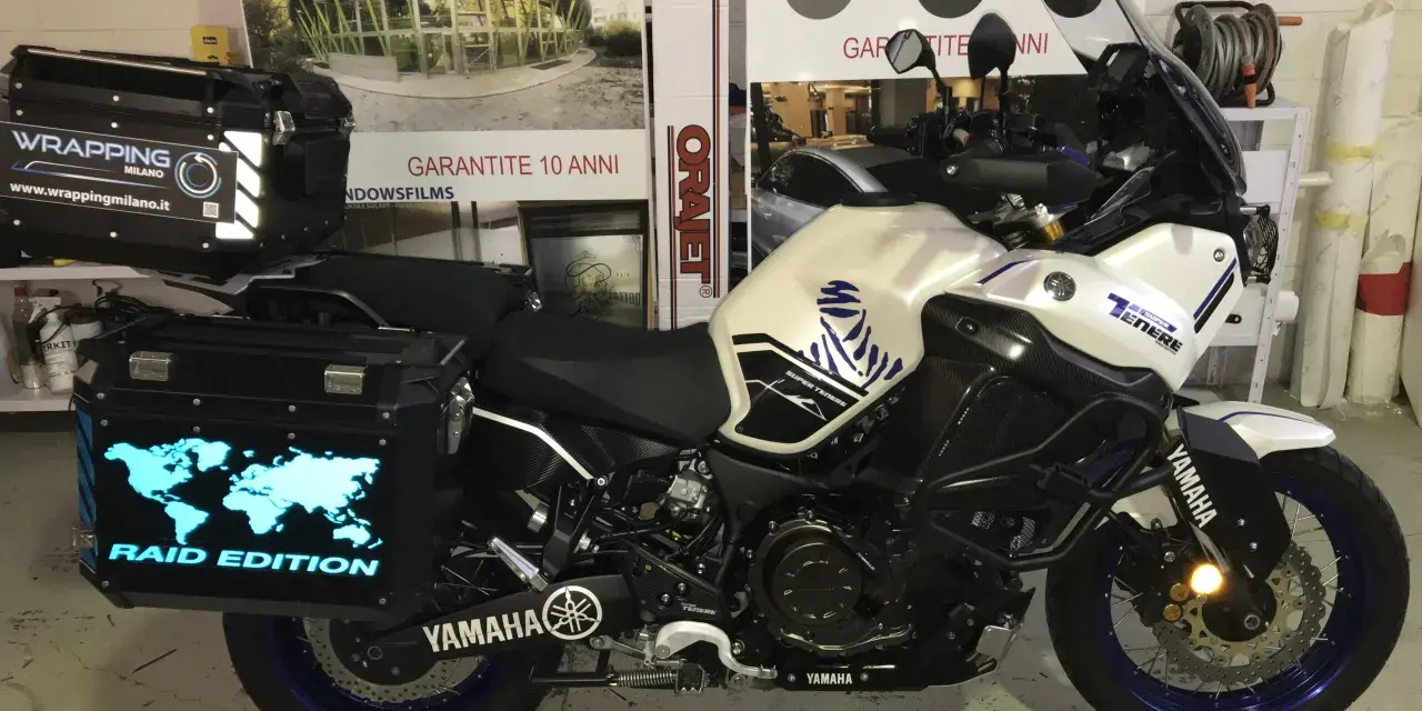 Moto Yamaha Super Ténéré con valigie personalizzate, una con mappa del mondo luminosa e scritta "Raid Edition". Il wrapping con acqua è un'idea per proteggere la moto.