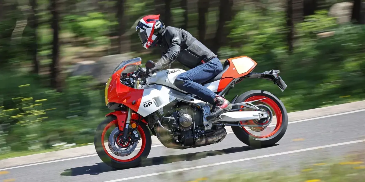 Un motociclista sfreccia su una Yamaha XSR900 GP, con il paesaggio sfocato dallo sfondo verde e giallo.