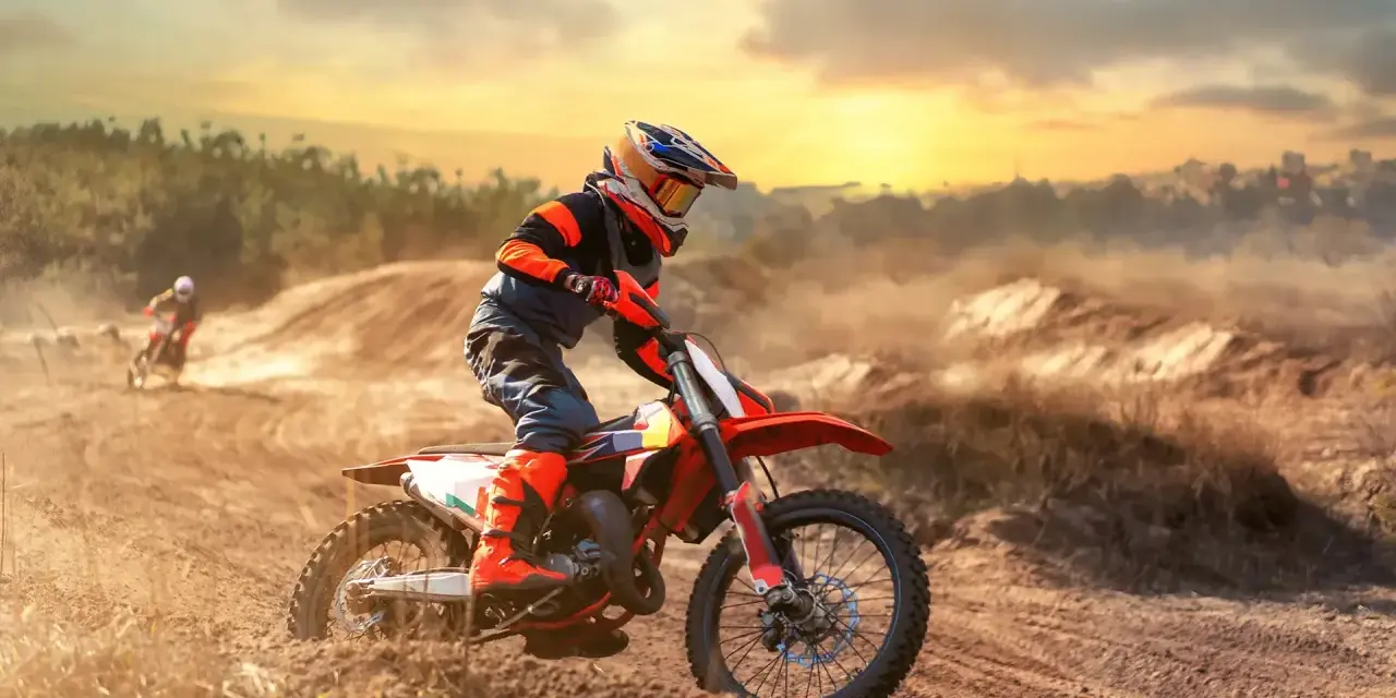 Un pilota di **enduro motocross** sfreccia su un terreno polveroso al tramonto, sollevando terra.