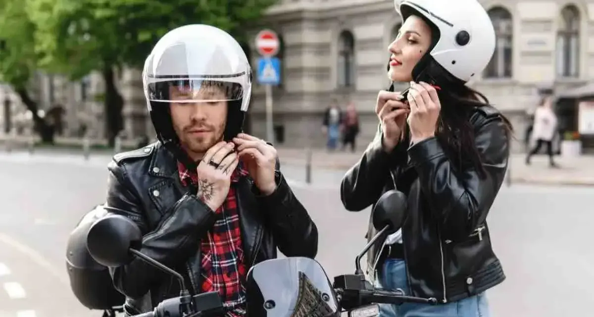 Coppia in moto, entrambi indossano un casco integrale. Lui con camicia a quadri, lei con giacca di pelle.