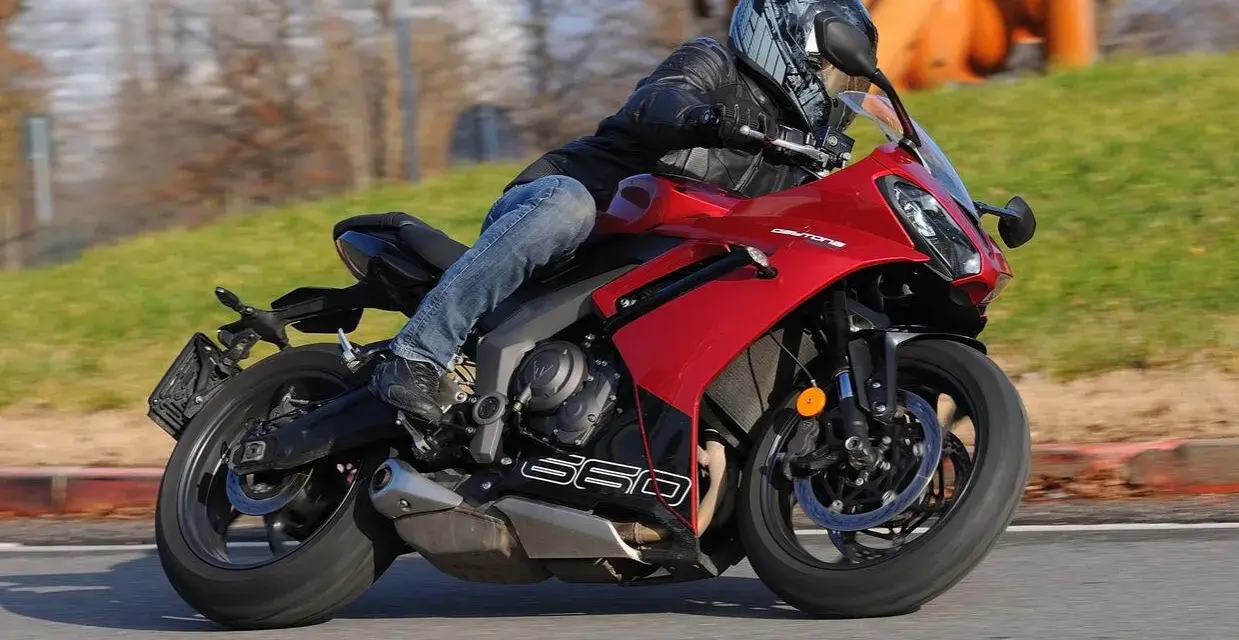Un motociclista sfreccia su una moto sportiva rossa, tra le migliori moto sportive, con un casco moderno e jeans.