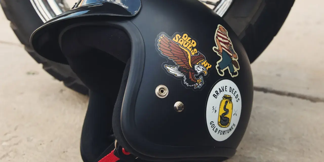 Casco nero con adesivi: un'aquila, un personaggio a strisce e un serpente in un barattolo. Si possono attaccare adesivi sul casco per personalizzarlo.