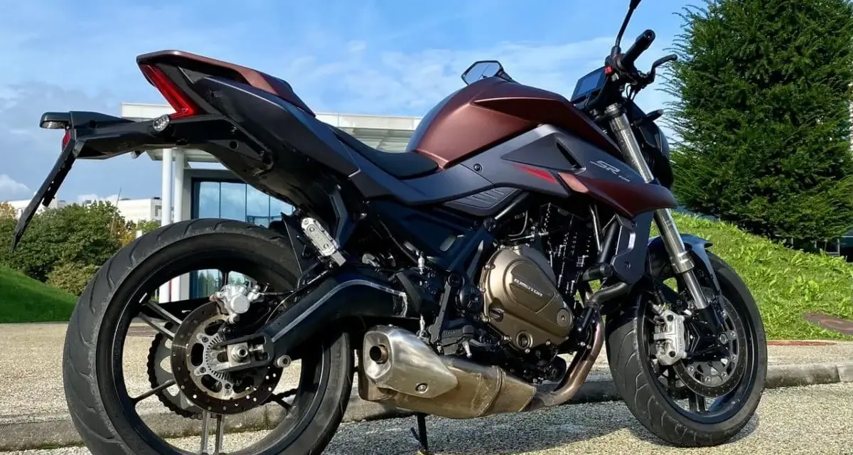 Moto SRK 700 color bronzo e nero, parcheggiata all'aperto con cielo azzurro e verde.