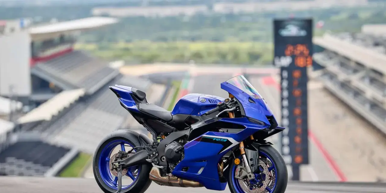 Yamaha R9, blu, su un cavalletto, con sfondo di un circuito. Dettagli tecnici da scoprire.