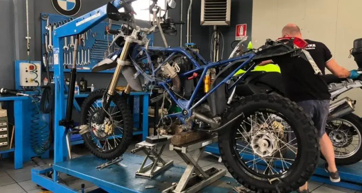 Officina BMW: moto smontata su sollevatore, in attesa del raffreddamento motore. Attrezzi e meccanico al lavoro.