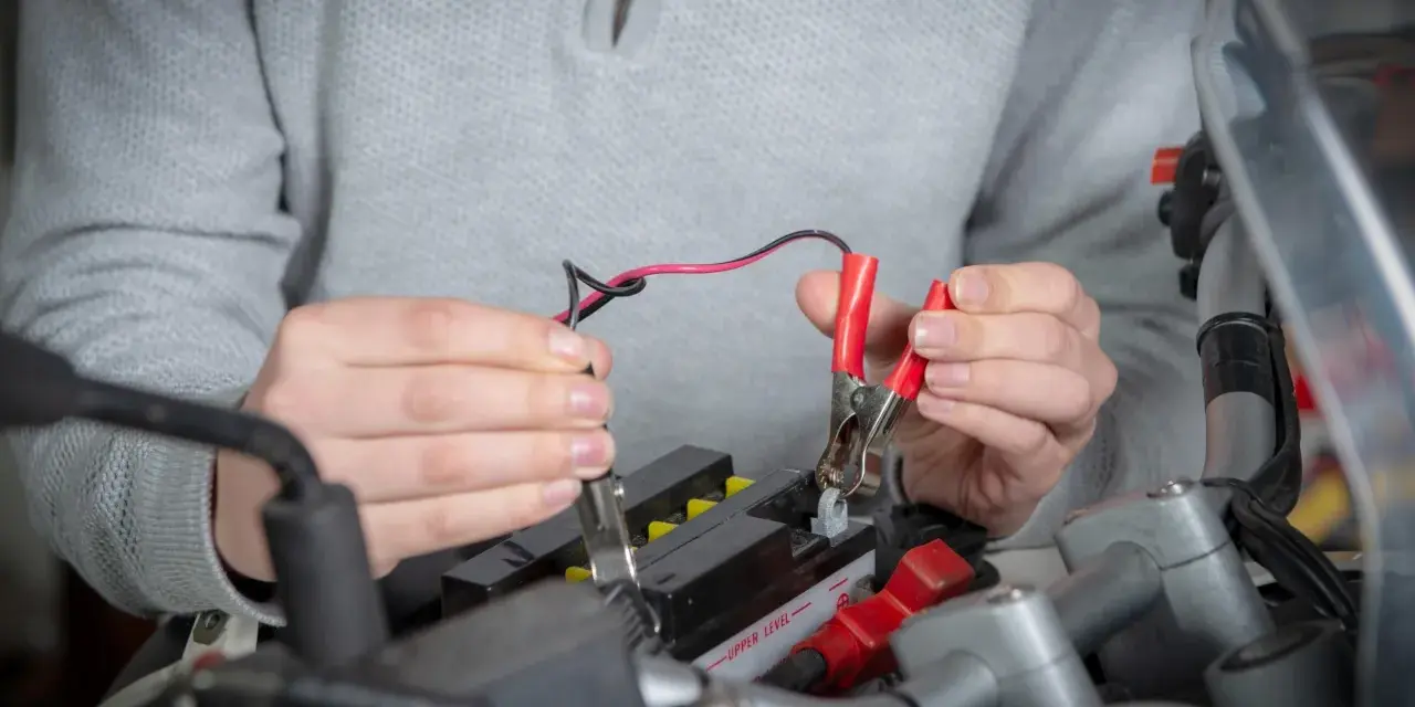 Mani che collegano i cavi a una batteria da moto ferma per ricaricarla.