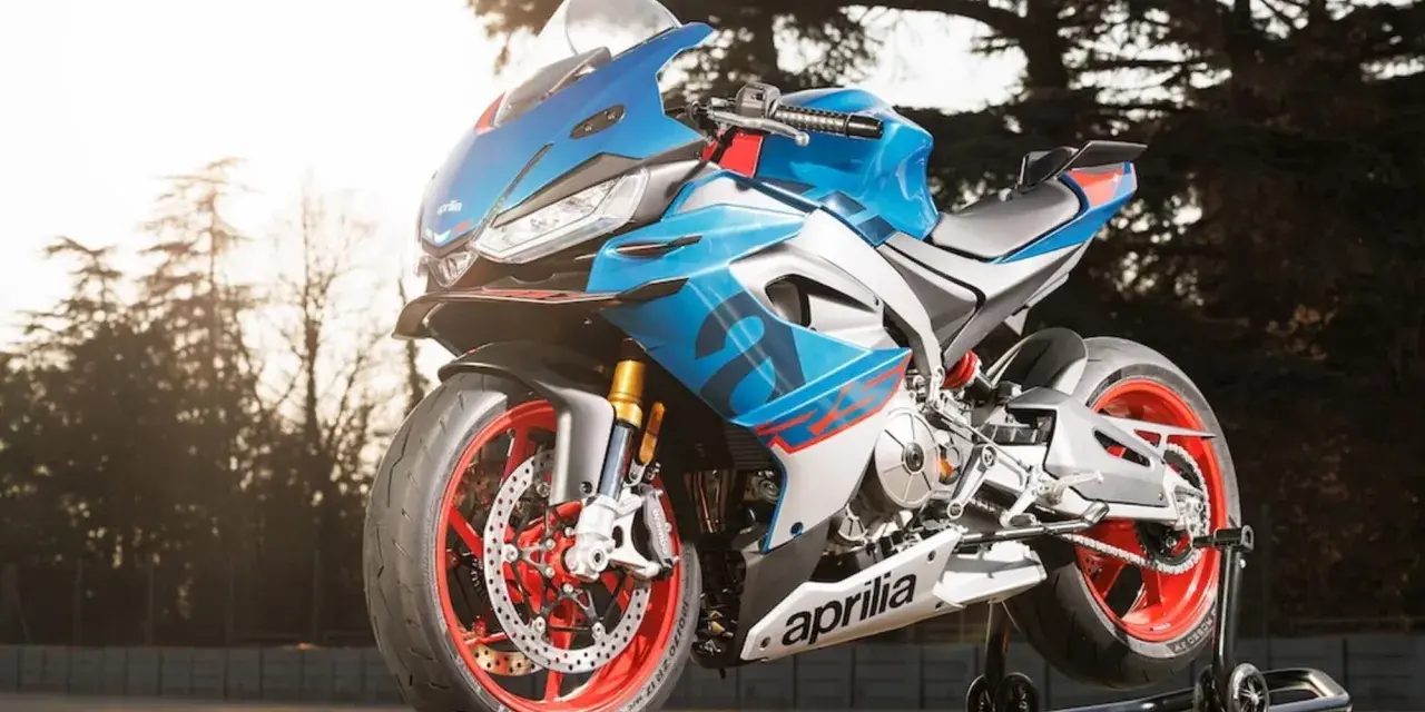 Aprilia carenata blu e rossa, con cerchi rossi, pronta per sfrecciare su pista.