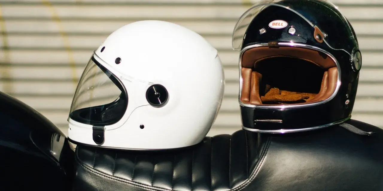 Due caschi integrali, uno bianco e uno nero, appoggiati sul sedile di una moto. Il peso del casco integrale è un fattore importante per il comfort.