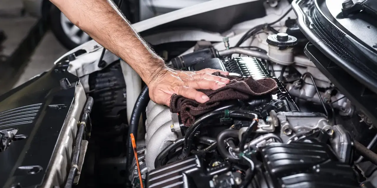 Mano che pulisce il motore dell'auto con un panno scuro, parte di un lavaggio motore accurato.