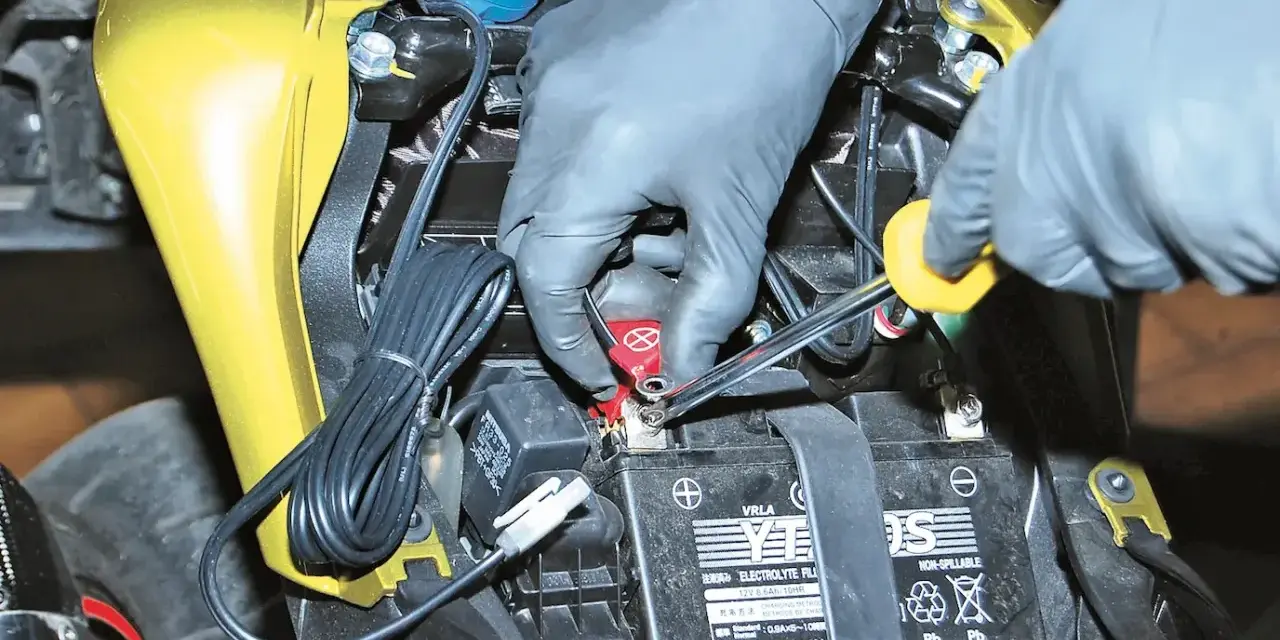 Mani guantate collegano un mantenitore di carica moto sempre collegato alla batteria.