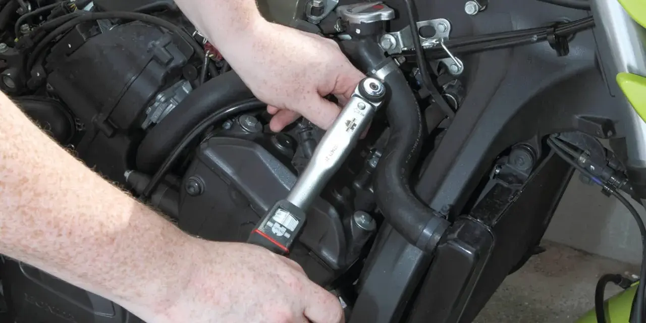 Mani che usano una chiave dinamometrica per il cambio candele di una moto.