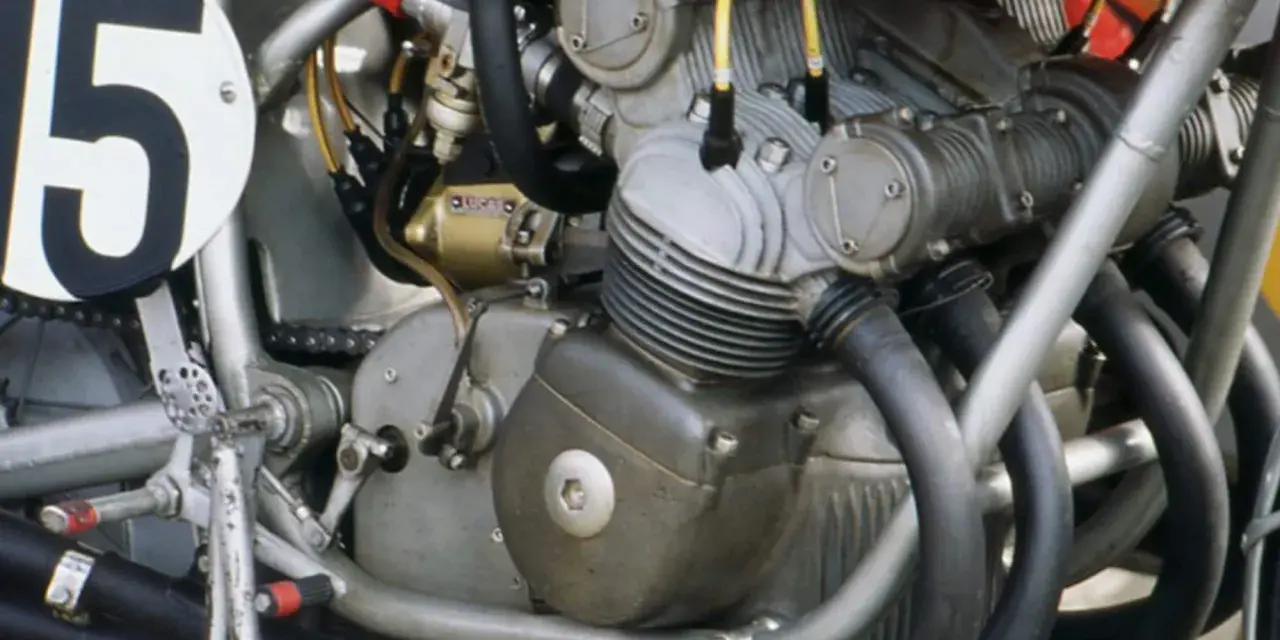 Dettaglio del motore di una moto da corsa, con il numero 15 su un cerchio bianco. Il motore è un complesso di tubi e metallo, pronto a ruggire.
