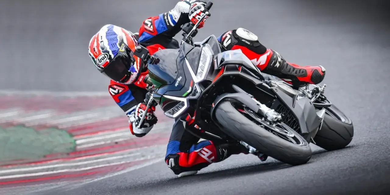 Un pilota in piega su una Aprilia Tuono 660 Factory, con tuta rossa e blu, affronta una curva su pista.