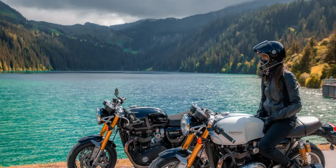Due moto da enduro, una nera e una bianca, con una donna in sella, godono del panorama di un lago alpino.