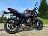 Moto SRK 700 color bronzo e nero, parcheggiata all'aperto con cielo azzurro e verde.
