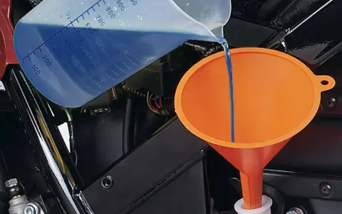 Versando liquido refrigerante blu in un imbuto arancione per diluirlo.