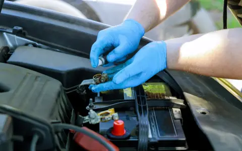 Mani con guanti blu puliscono i contatti arrugginiti della batteria rosso e nero dell'auto.