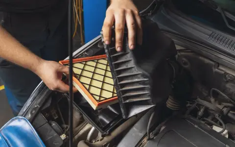 Mani che sostituiscono un filtro aria sporco nel vano motore di un'auto.