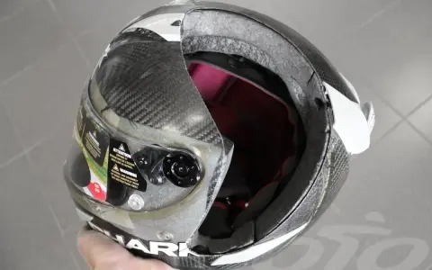 Casco da moto con calotta in fibra di carbonio e abs o policarbonato, visiera trasparente e interni rossi. La calotta presenta una crepa.